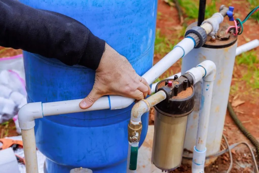 Technician connecting PVC plumbing to a blue well pressure tank and sediment filter