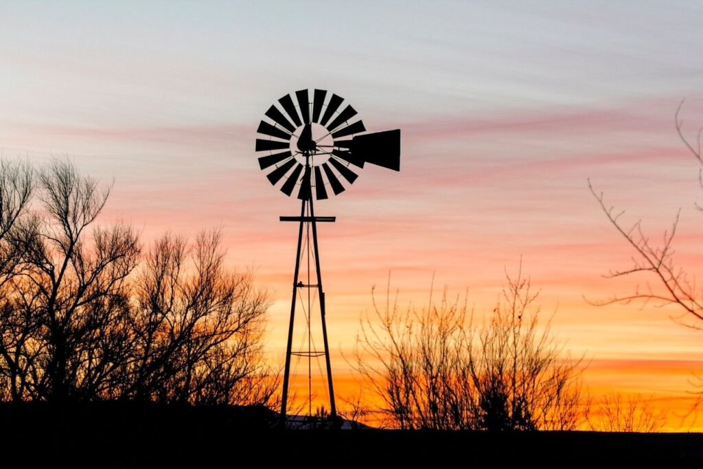 Farm windmill silhouetted against an orange sunset sky